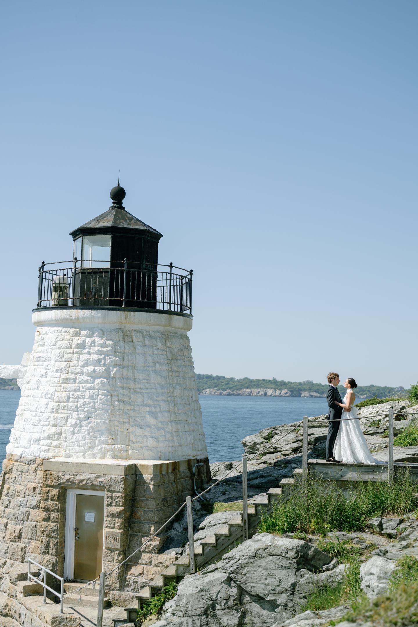 Lighthouse by the sea with couple standing on steps, bright sunny day.