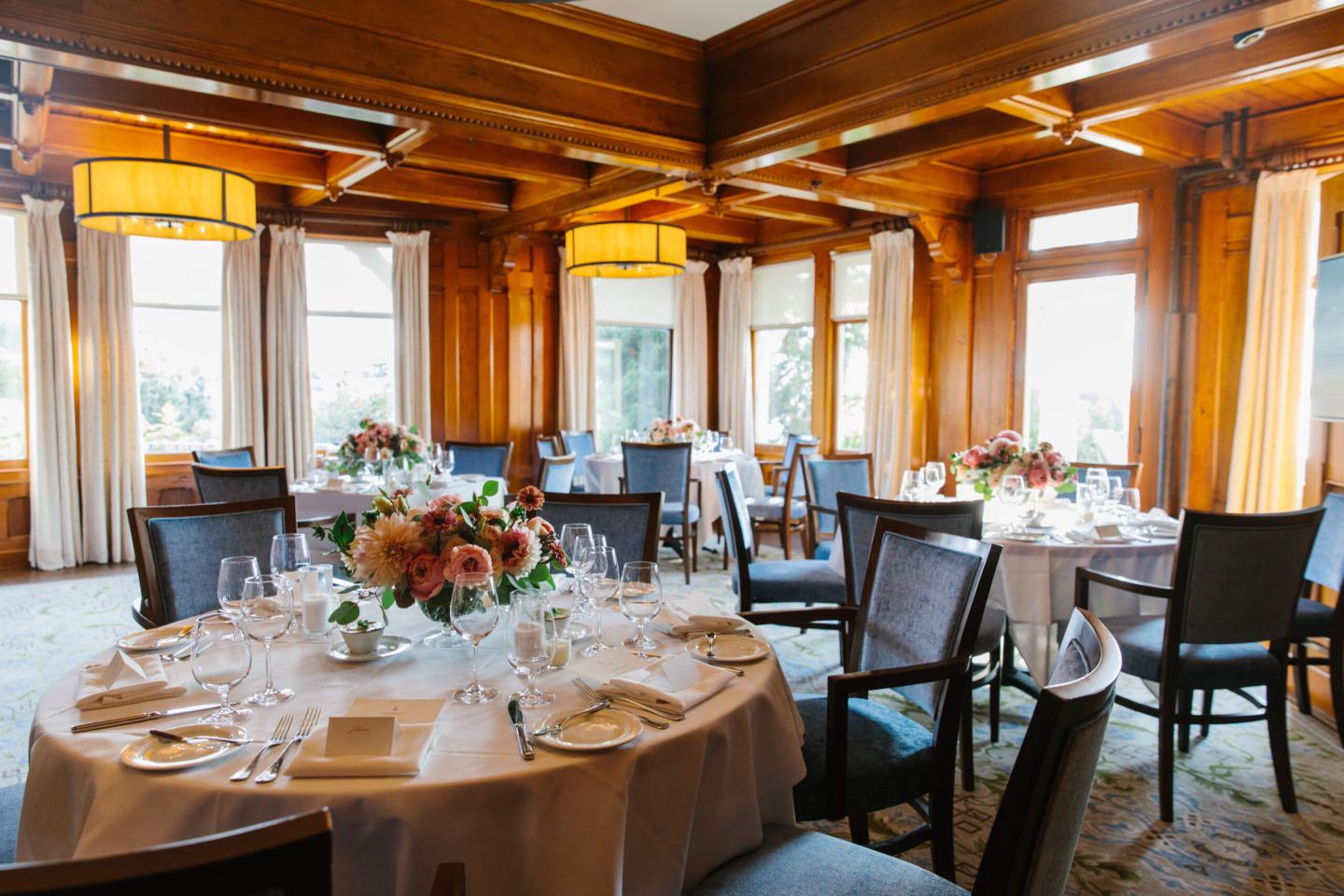 Elegant dining room with round tables, floral centerpieces, and wooden walls.