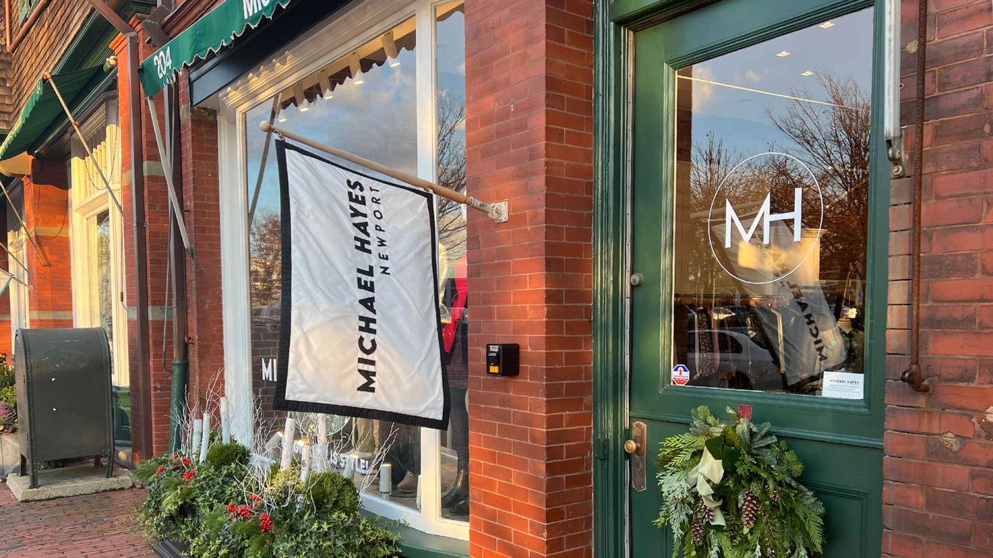 Brick storefront with a green door and festive wreath, flag hanging outside.