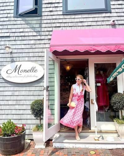 Woman in pink dress standing in shop doorway with pink awning.