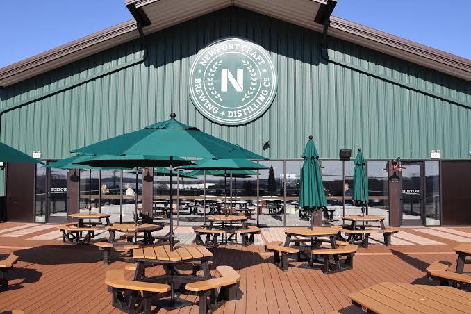 Green building exterior with round tables and umbrellas on a sunny patio.