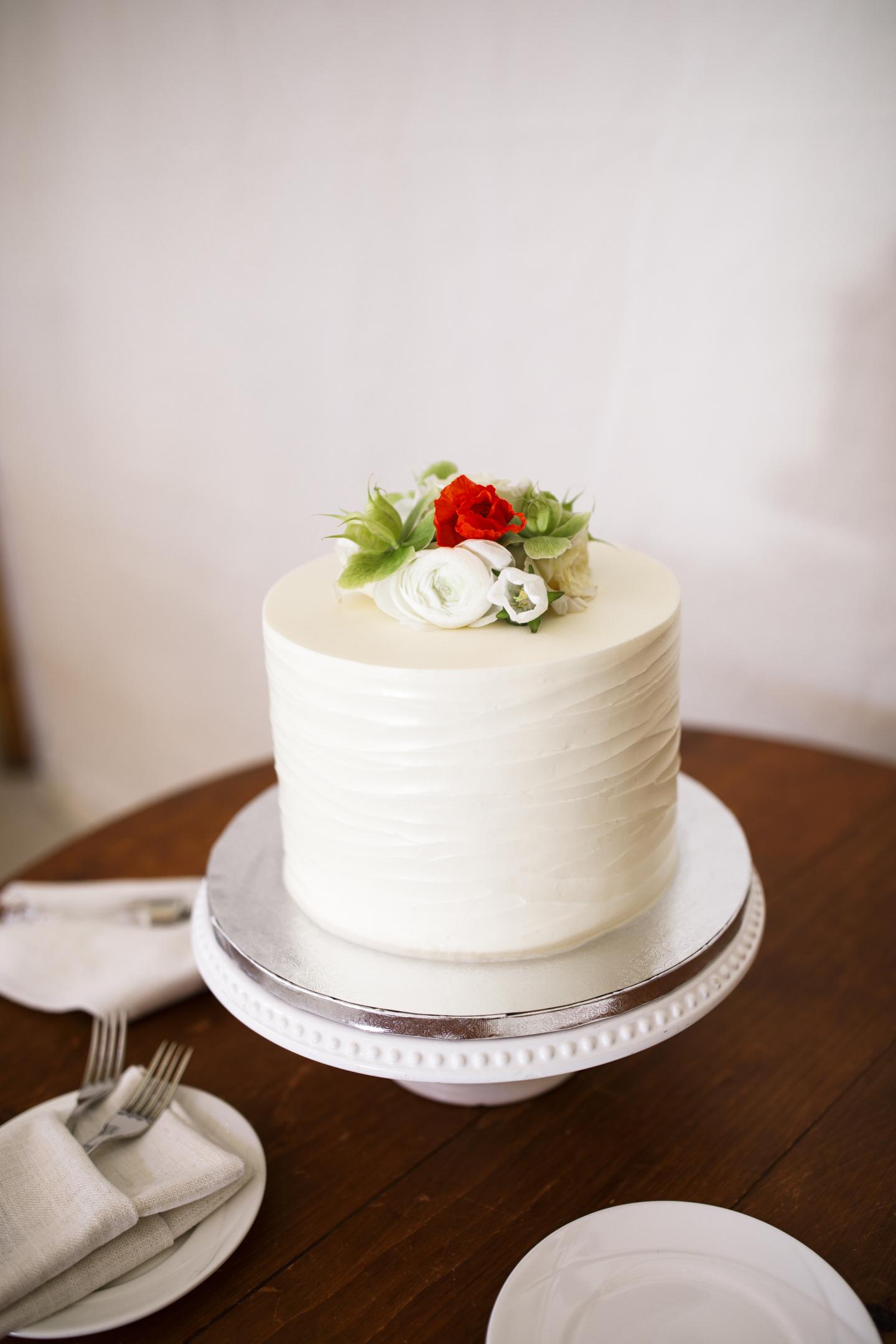 White frosted cake with red and white flowers on top, on a wooden table.