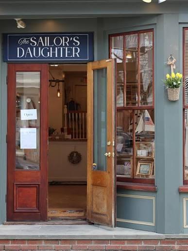 Storefront with open wooden door and flowers by the window.