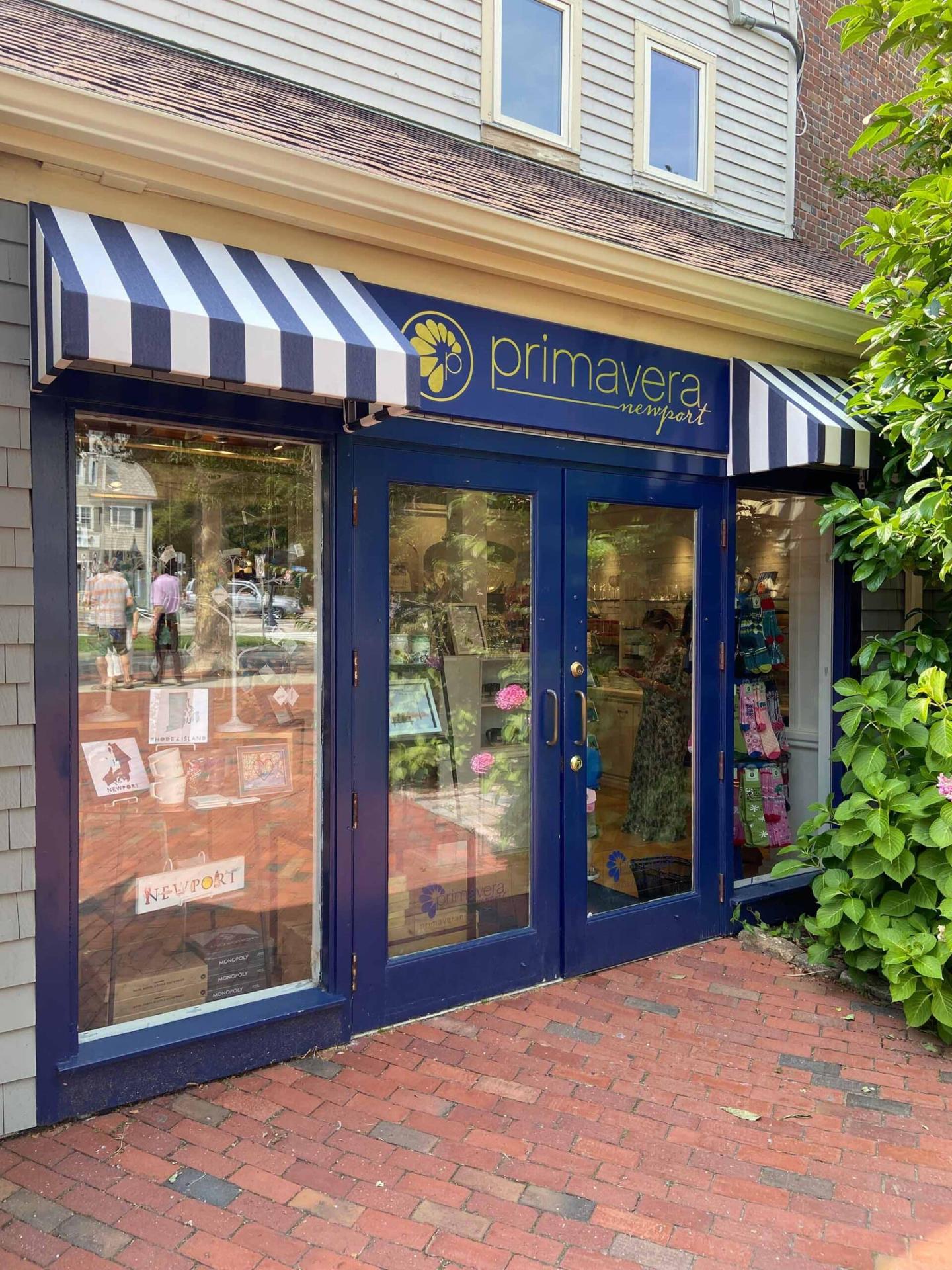 Storefront with blue doors and striped awning, brick sidewalk in front.