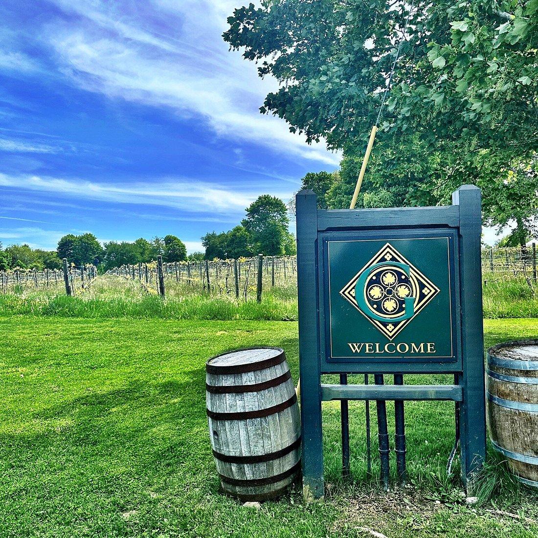 Welcome sign in a vineyard with blue sky and oak barrels.