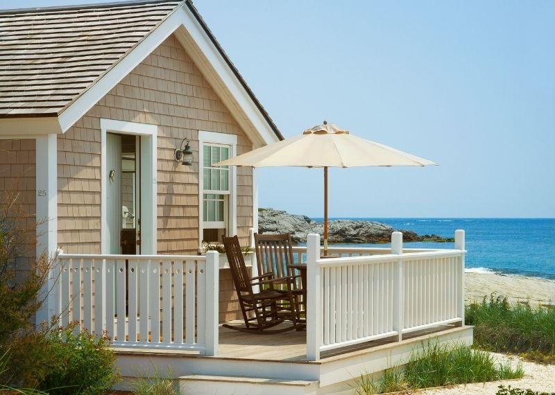 Beach house with umbrella on deck overlooking sandy beach and rocks at Castle Hill Inn in Newport, RI