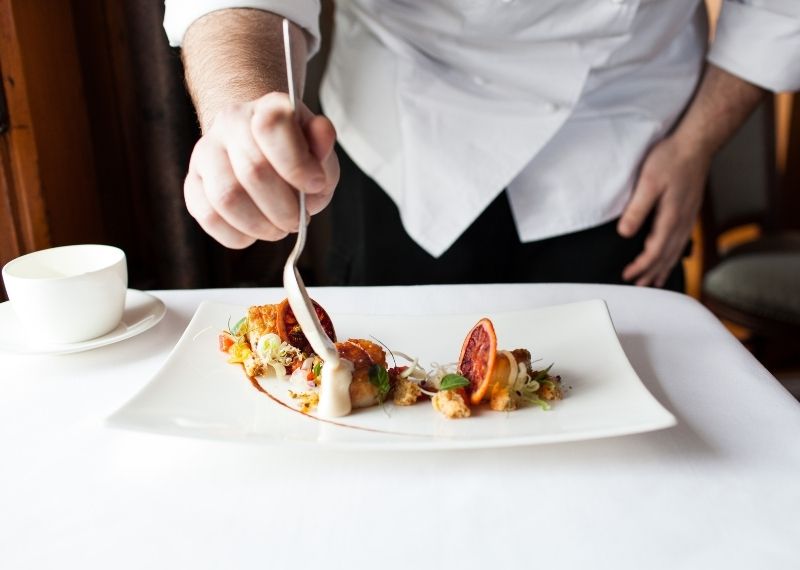 Man pouring white sauce onto food dish on plate at Castle Hill Inn in Newport, RI