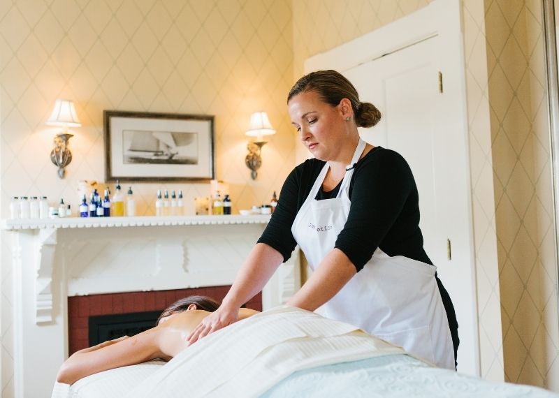 Woman in apron giving a massage to woman on table in front of massage oils on top of table at Castle Hill Inn in Newport, RI