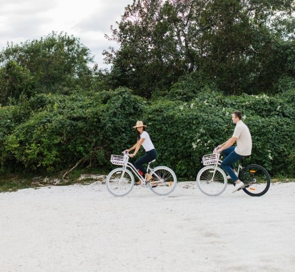 Two people riding bicycles on sand near trees and shrubbery at Castle Hill Inn in Newport, RI