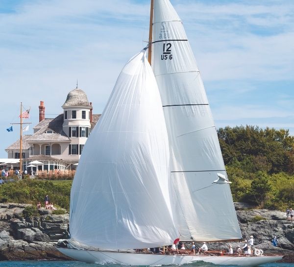 Sailboat on water with people in it near rocky beach in front of Castle Hill Inn in Newport, RI