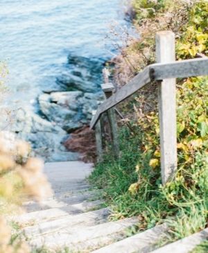 Stairs covered in sand leading to beach near ocean with railing at Castle Hill Inn in Newport, RI