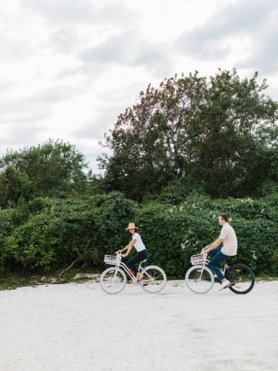 Two people riding bicycles on sand near trees and shrubbery at Castle Hill Inn in Newport, RI