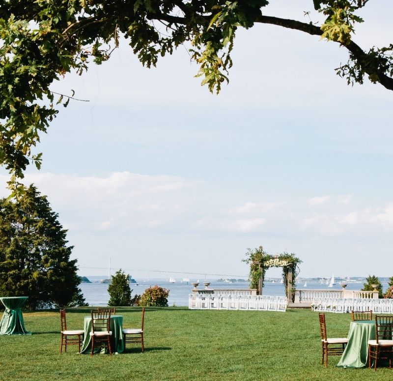 Wedding setup near ocean with white chairs and tables under a tree at Castle Hill Inn in Newport, RI