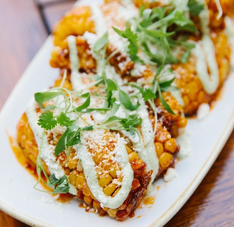 Plate of street corn on white plate topped with cheese and white sauce at Castle Hill Inn in Newport, RI