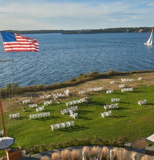 White lawn chairs overlooking the ocean with American flag blowing in breeze at Castle Hill Inn in Newport, RI
