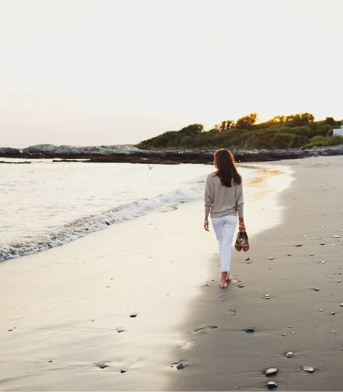 Woman holding shoes walking on sandy beach at sunset at Castle Hill Inn in Newport, RI