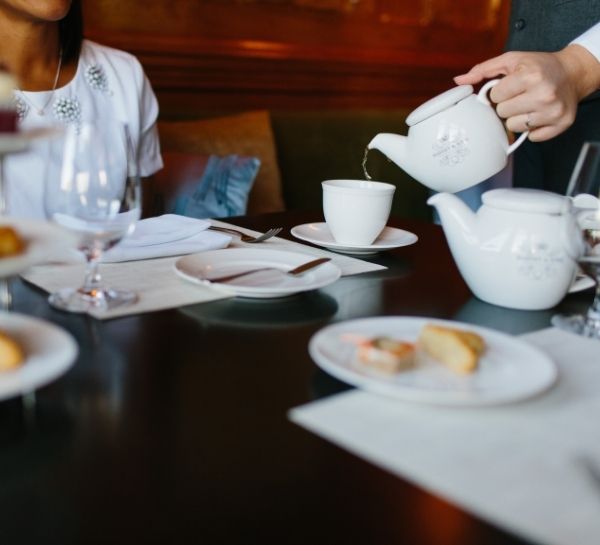 Person pouring tea into teacup with people at table at Castle Hill Inn in Newport, RI