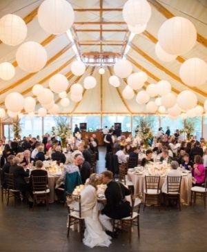 Wedding tent with large white balloons hanging from ceiling and people in wedding attire underneath and bride and groom kissing in front at Castle Hill Inn in Newport, RI