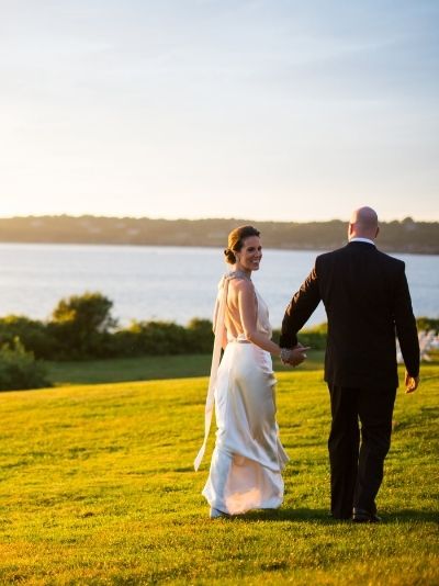Man and woman in wedding attire holding hands near ocean at Castle Hill Inn in Newport, RI