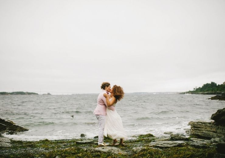 Two people kissing near ocean on rocky beach at Castle Hill Inn in Newport, RI