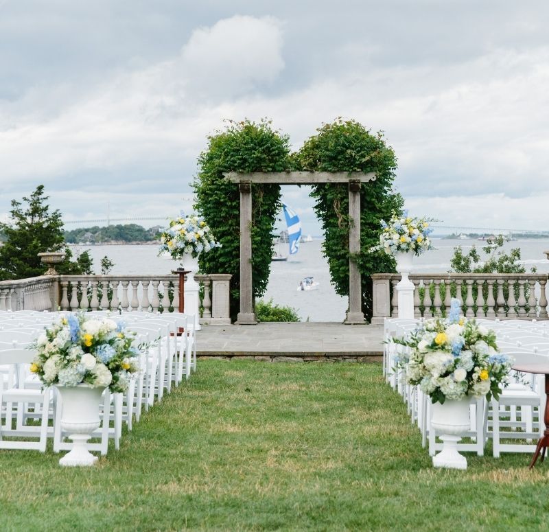 Wedding arch near stone pillars in front of white chairs in front of ocean at Castle Hill Inn in Newport, RI