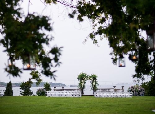 Wedding setup overlooking ocean under trees in front of white chairs at Castle Hill Inn in Newport, RI